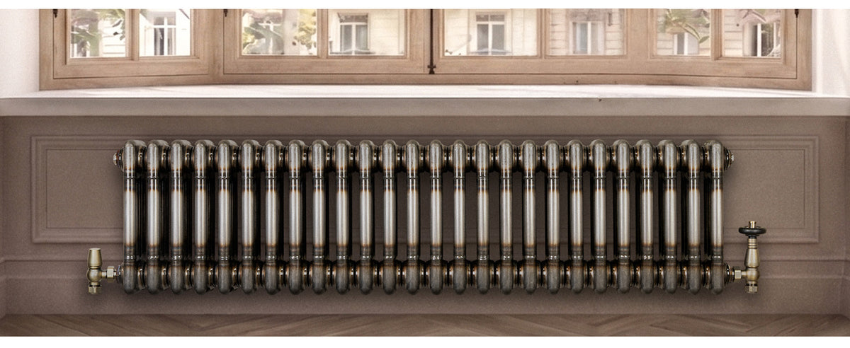 Stijlvolle metalen radiator met een glanzende afwerking, geplaatst onder een grote raam met houten kozijnen en een lichte vloer