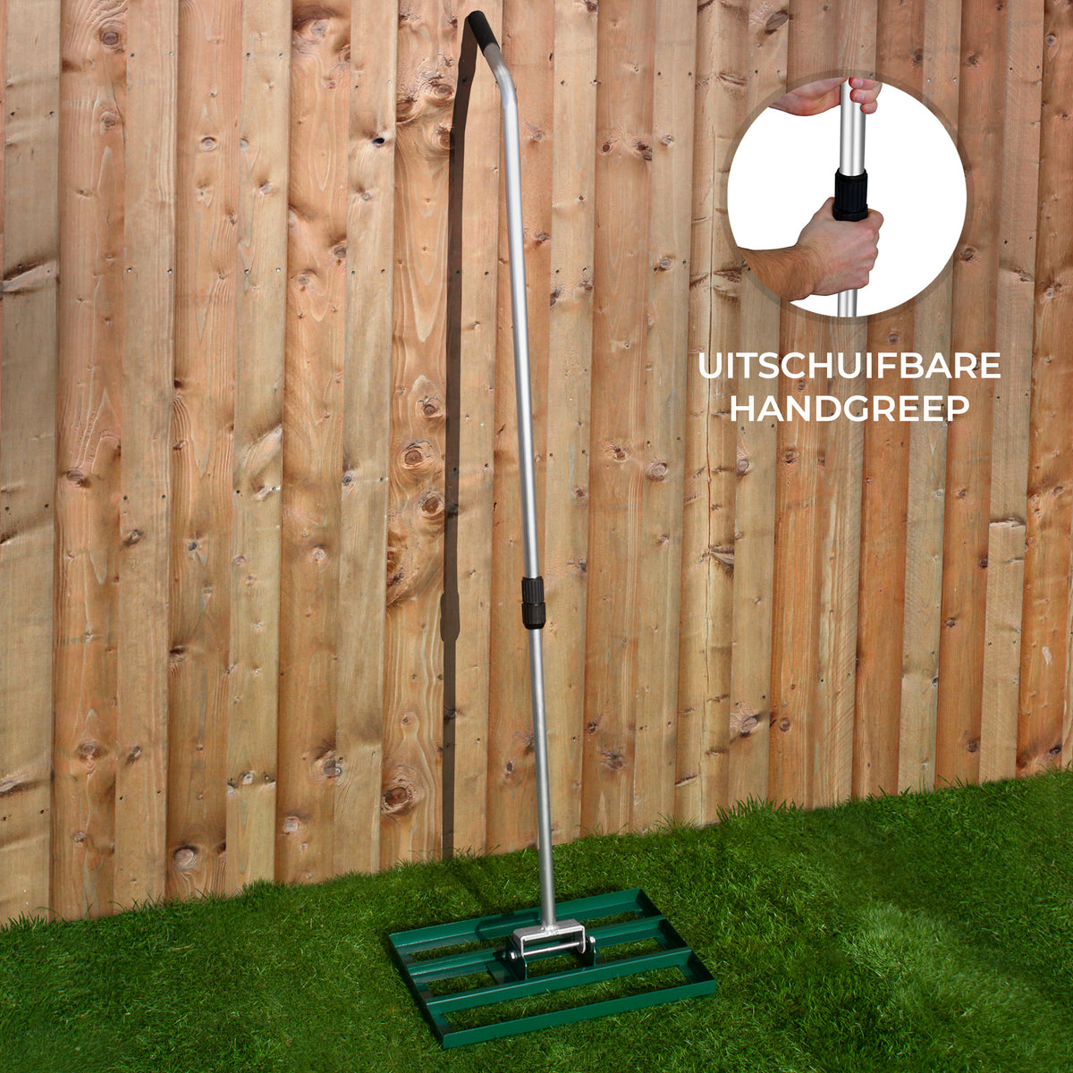 Groene T-MECH gazon nivellering hark van 50 cm met een uitschuifbare handgreep, geplaatst op een grasveld tegen een houten schutting