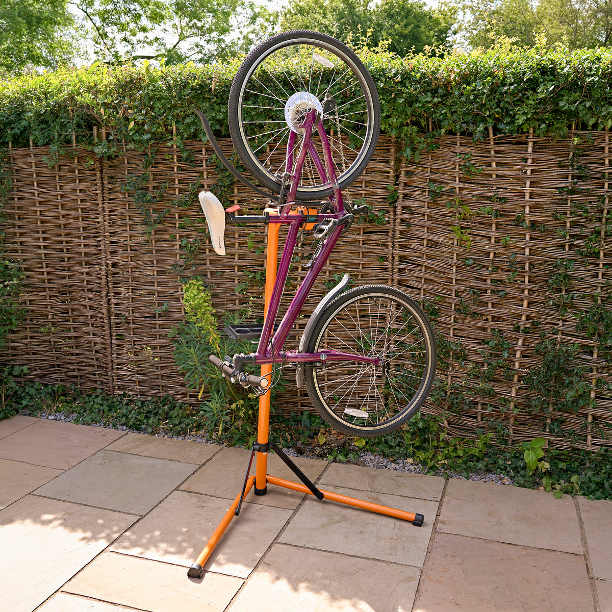 Fiets montagestandaard met een oranje en zwarte basis, ondersteunt een fiets met een paarse frame, ideaal voor onderhoud en reparatie