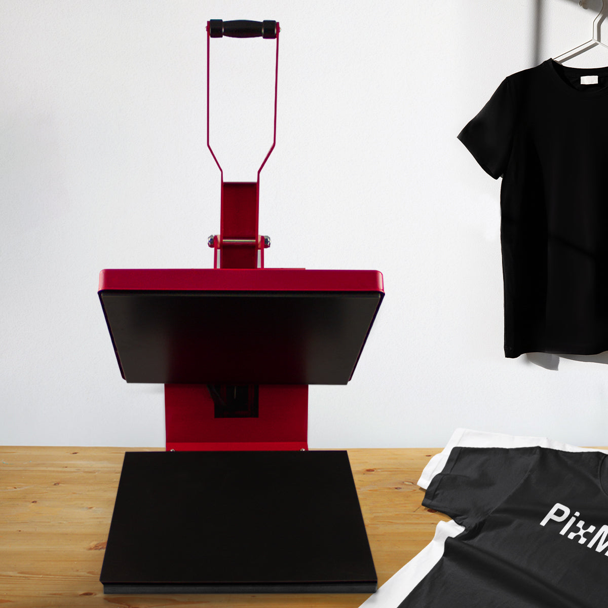 Rode hittepers met een zwart drukvlak van 38x38 cm, naast een zwarte en grijze T-shirt, op een houten tafel