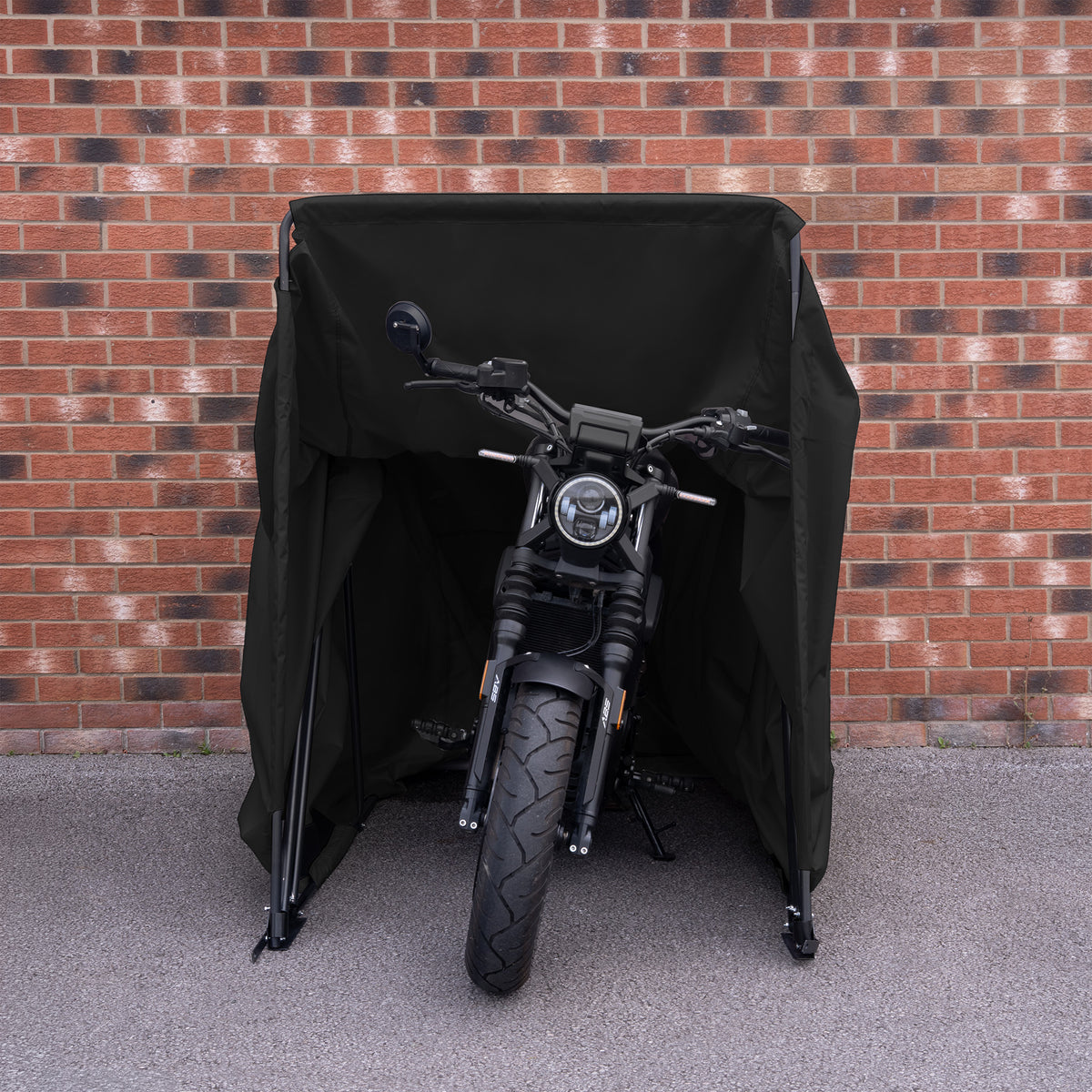 Zwarte motorfiets bedekt met een stevige, waterdichte hoes, geplaatst tegen een bakstenen muur voor bescherming en stijl