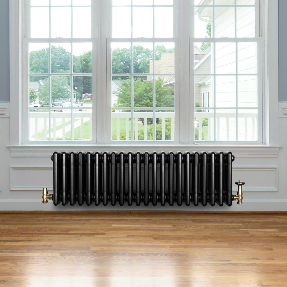 Traditionele zwarte 4-kolom radiator van 300 x 1010 mm met haakse thermostaatkraan, geplaatst onder een groot raam op houten vloer