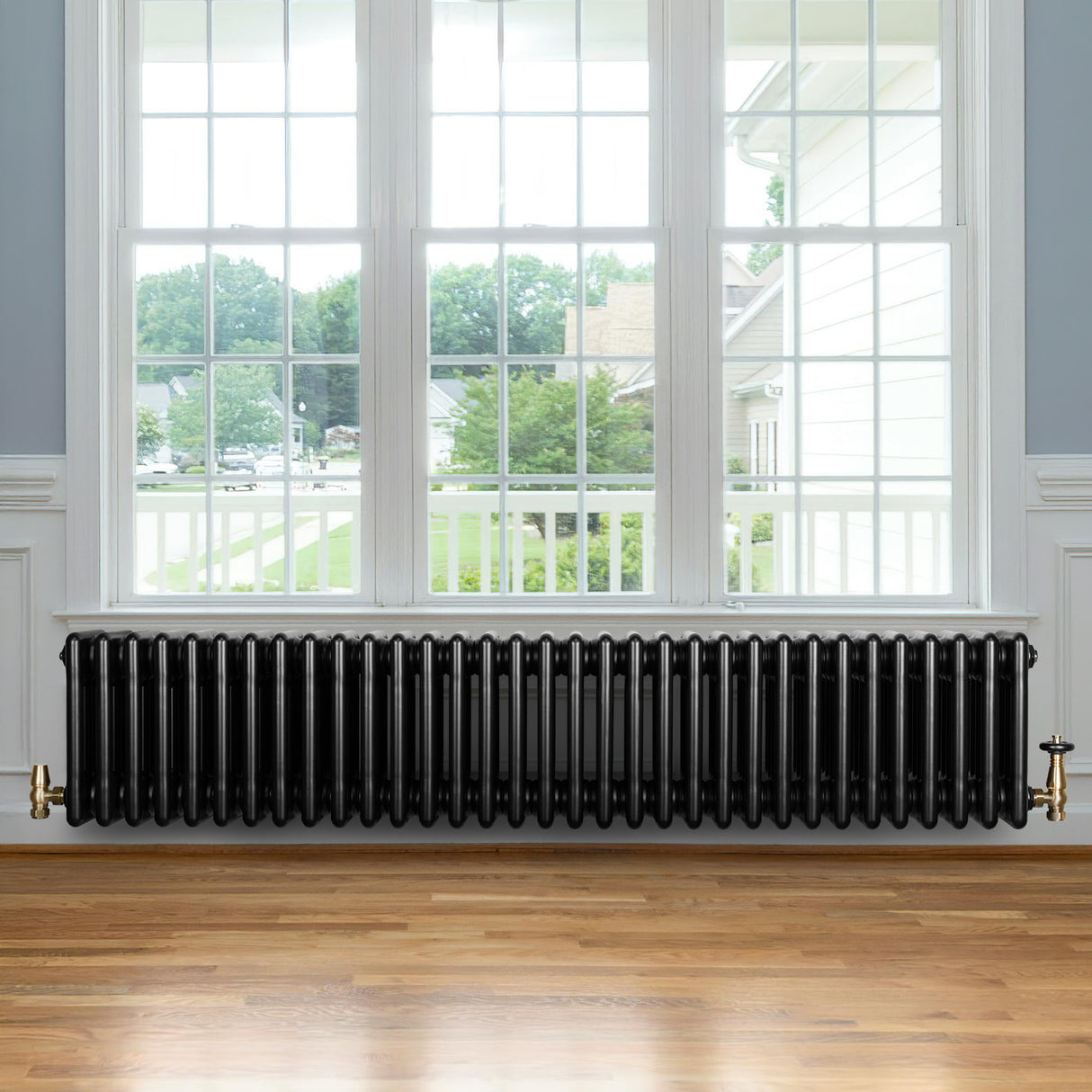 Traditionele zwarte 4-kolom radiator van 300 x 1505 mm met een haakse thermostaatkraan, geplaatst onder een groot raam