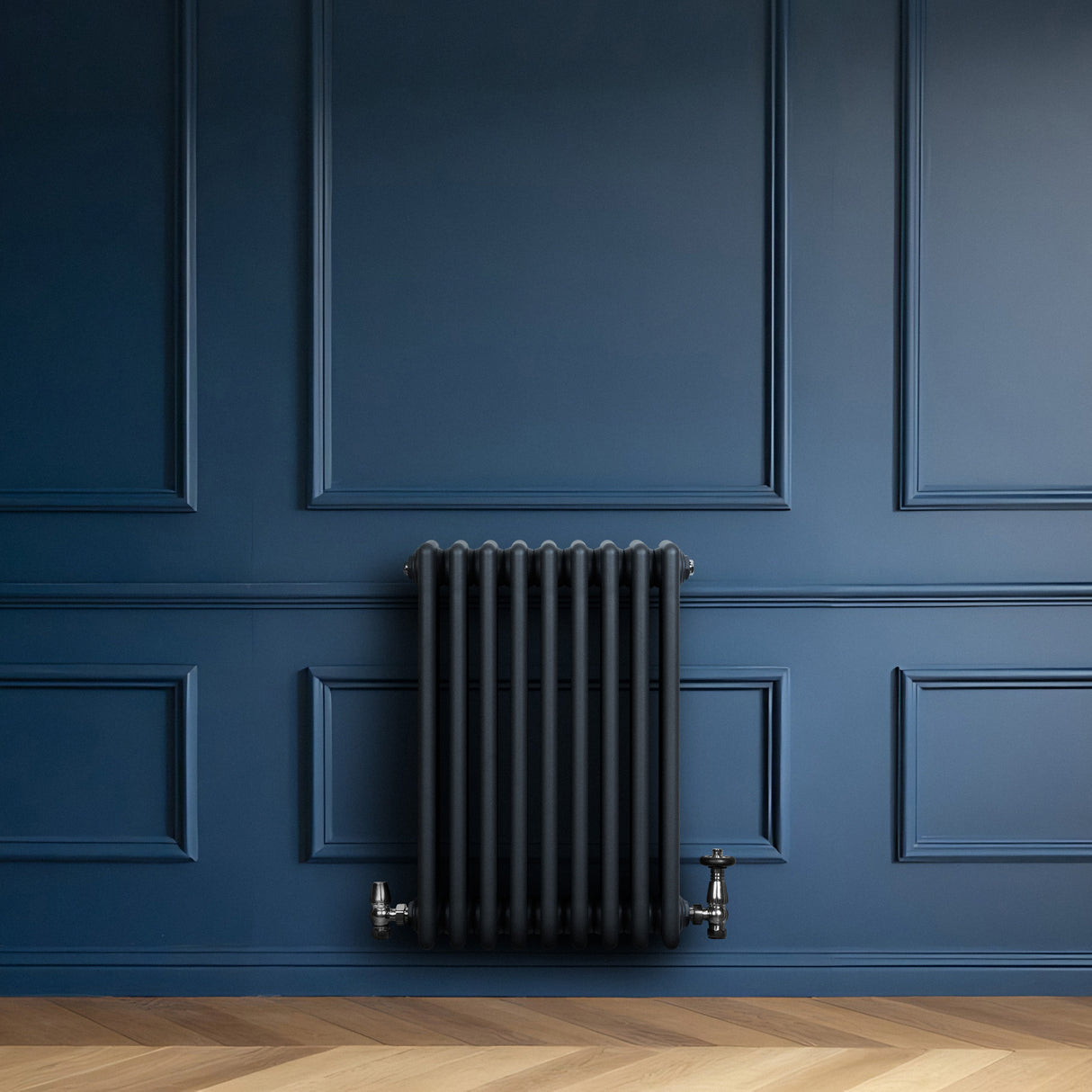 Traditionele antraciet grijze 4-kolom radiator met haakse thermostaatkraan, geplaatst tegen een diepblauwe wand