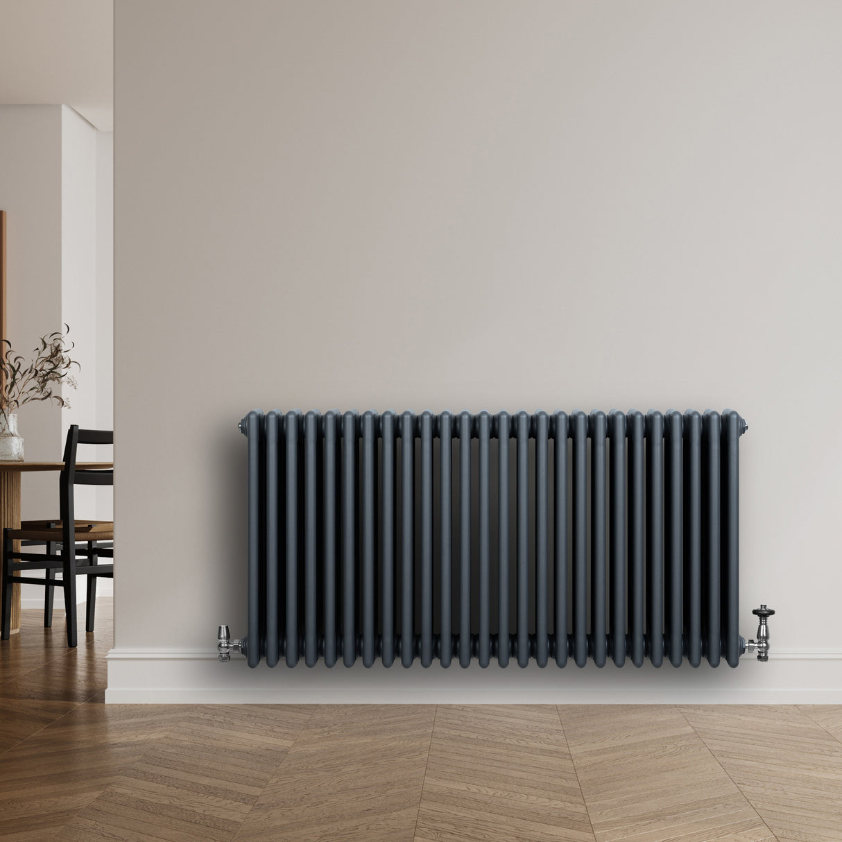 Traditionele antraciet grijze 4-kolom radiator van 600 x 1190 mm met haakse thermostaatkraan, geplaatst tegen een lichte muur