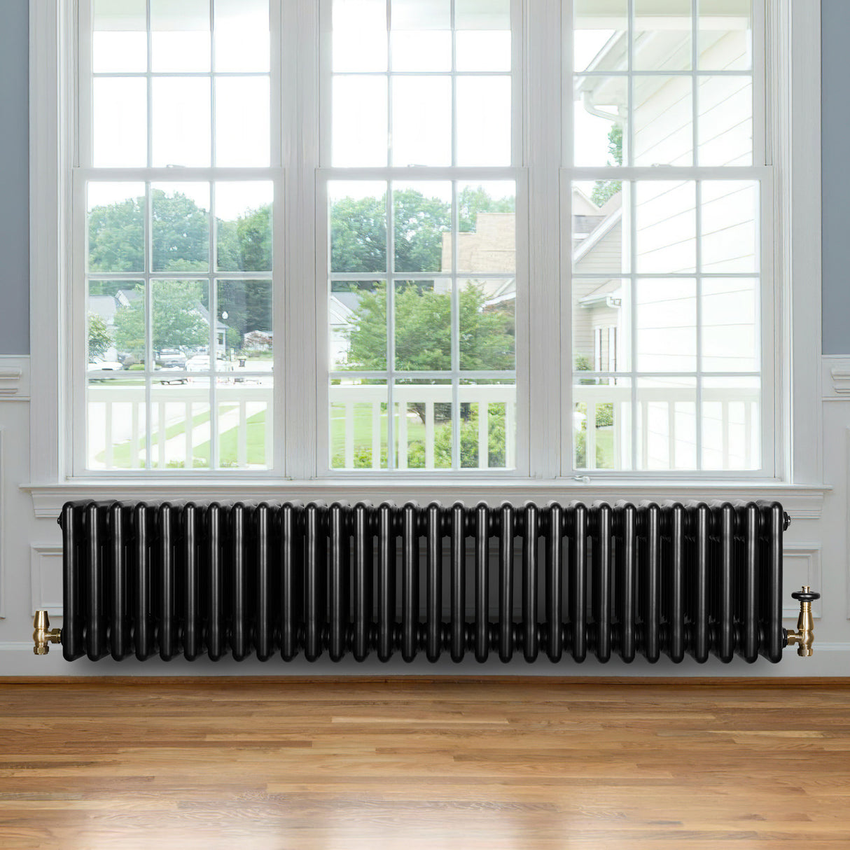 Traditionele zwarte 4-kolom radiator van 300 x 1370 mm met glanzende afwerking, geplaatst onder een groot raam in een lichte ruimte