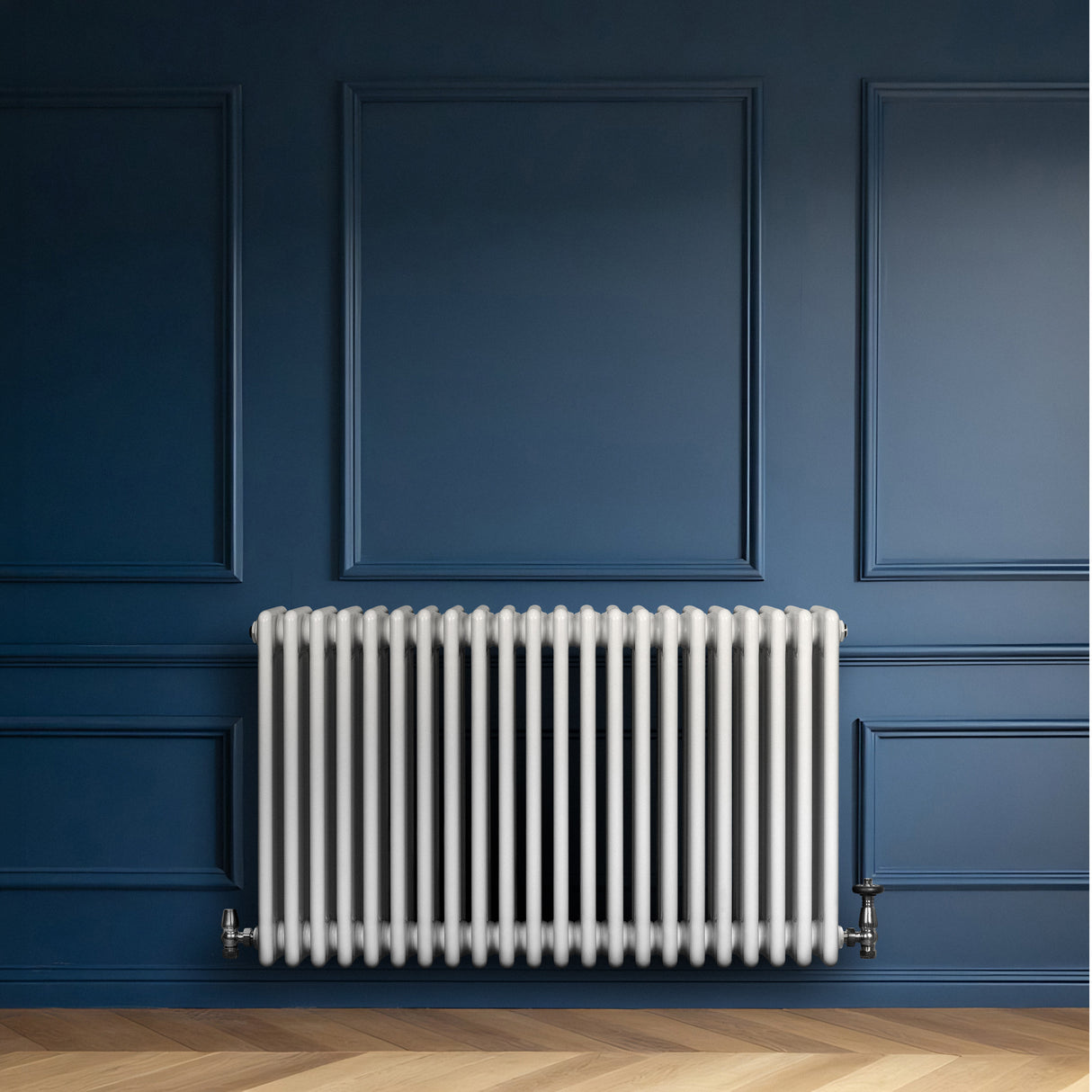 Traditionele witte 4-kolom radiator van 600 x 1010 mm tegen een donkerblauwe muur, met een strakke, glanzende afwerking en metalen aansluitingen