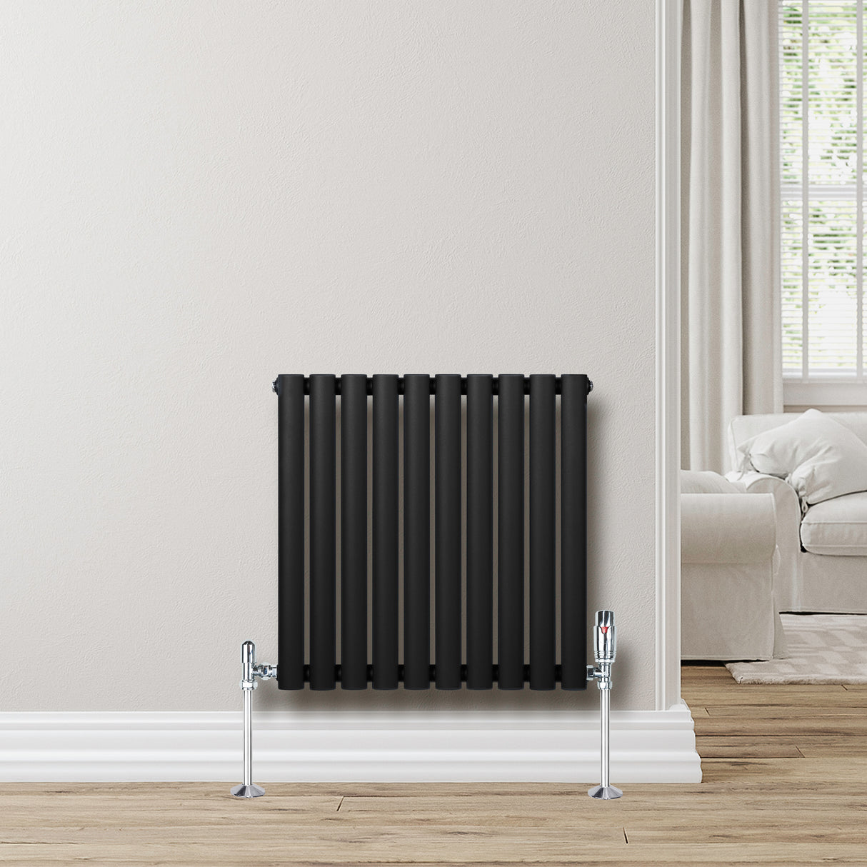 Ovale zwarte designradiator met één kolom, 600 mm x 600 mm, geplaatst tegen een lichte muur in een moderne woonkamer