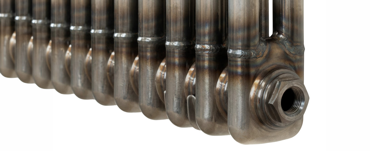 Gegolfde metalen radiatoren met een glanzende afwerking en zichtbare lasnaden, in een strakke rij geplaatst tegen een witte achtergrond