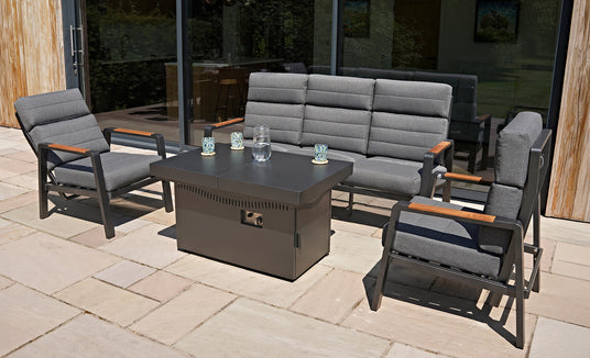 Moderne tuinset met grijze kussens, houten accenten en een zwart vuurtafel, geplaatst op een stenen terras met groene achtergrond
