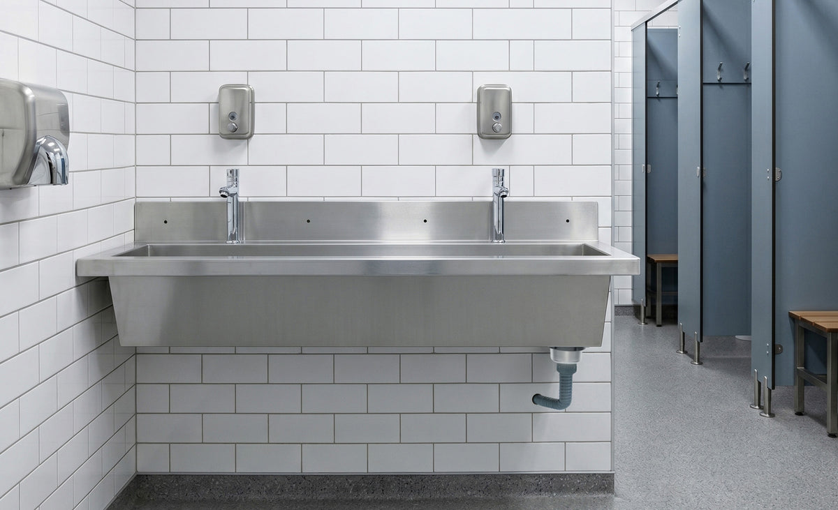 Roestvrijstalen wastafel met dubbele kranen, witte tegels op de muur en blauwe kleedhokjes op de achtergrond in een moderne ruimte