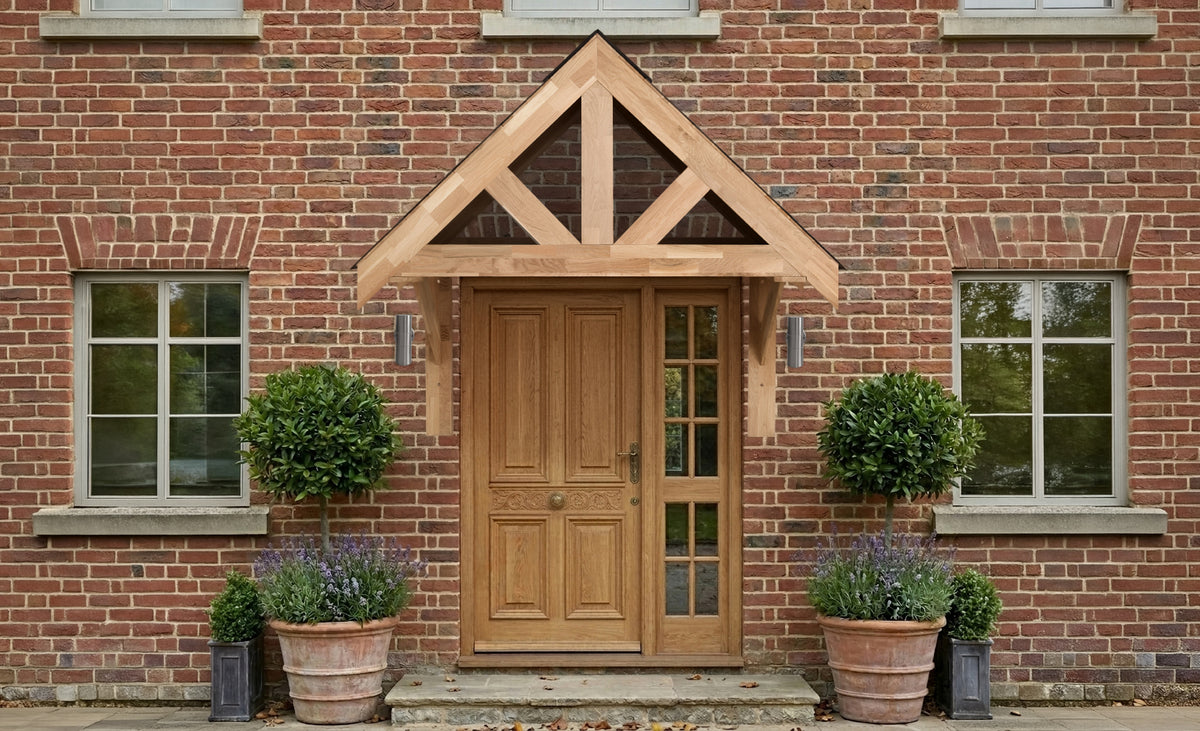 Houten voordeur met een moderne luifel, omringd door groene buxusplanten in terracotta potten voor een bakstenen muur