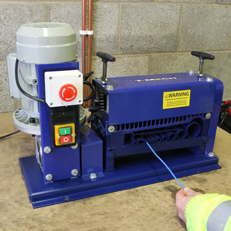 Robuuste blauwe draadstripmachine met motor, knoppen en waarschuwingslabel, geplaatst op een houten werkblad in een industriële omgeving