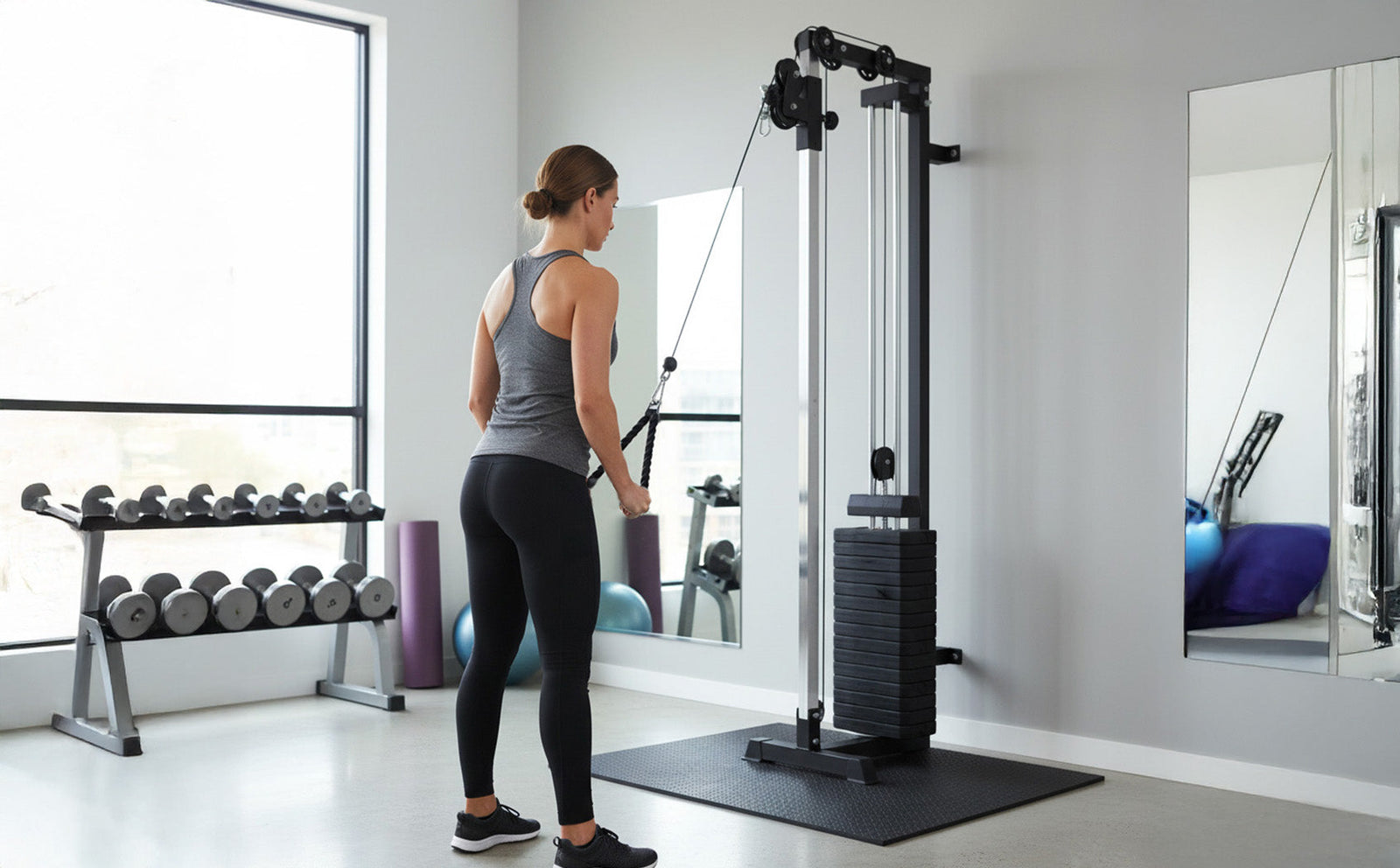 Vrouw in sportoutfit gebruikt wandgemonteerde kabel pulley in moderne home gym met gewichten en spiegel op de achtergrond