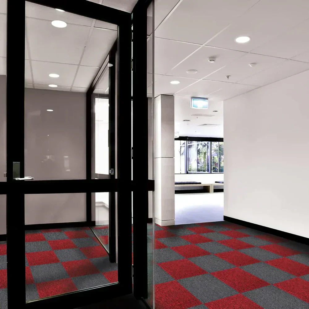 Een moderne gang met tapijttegels in een ruitpatroon van rood en grijs, omringd door glazen wanden en een strakke afwerking
