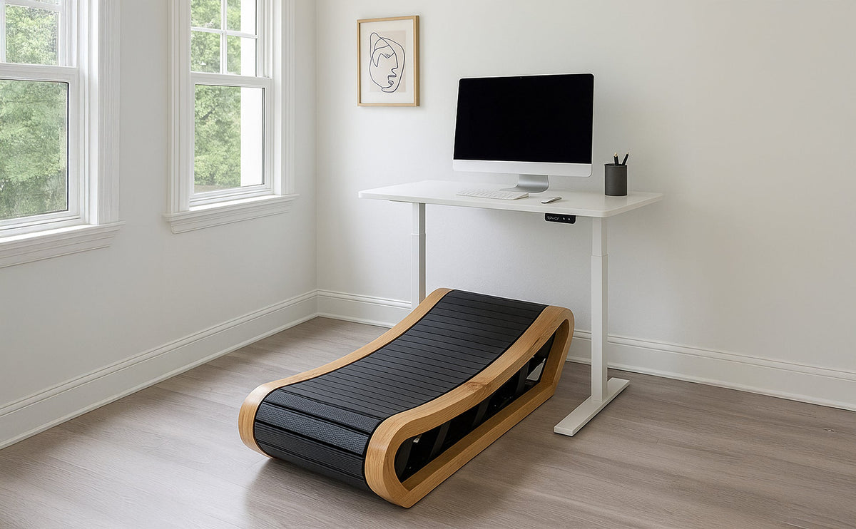 Een stijlvolle curved loopband met een houten frame en zwarte loopband, geplaatst naast een bureau met een computer in een lichte kamer