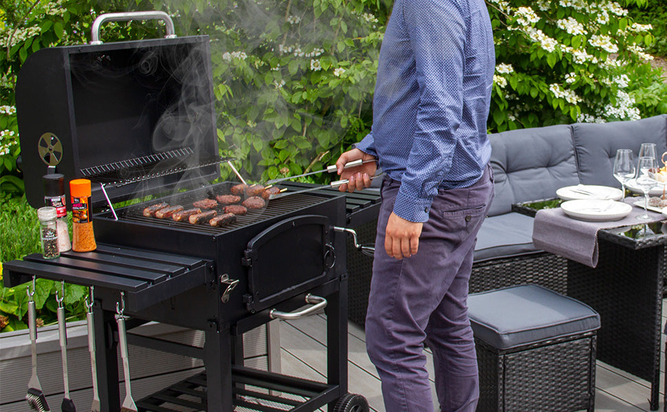 Een man in een blauw shirt grilt sappige worstjes op een zwarte barbecue, omringd door groene planten en een gezellige tuinsetting