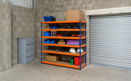 Kleurige stellingkast met oranje planken, gevuld met gereedschap, dozen en opslagcontainers in een garage met betonnen muren