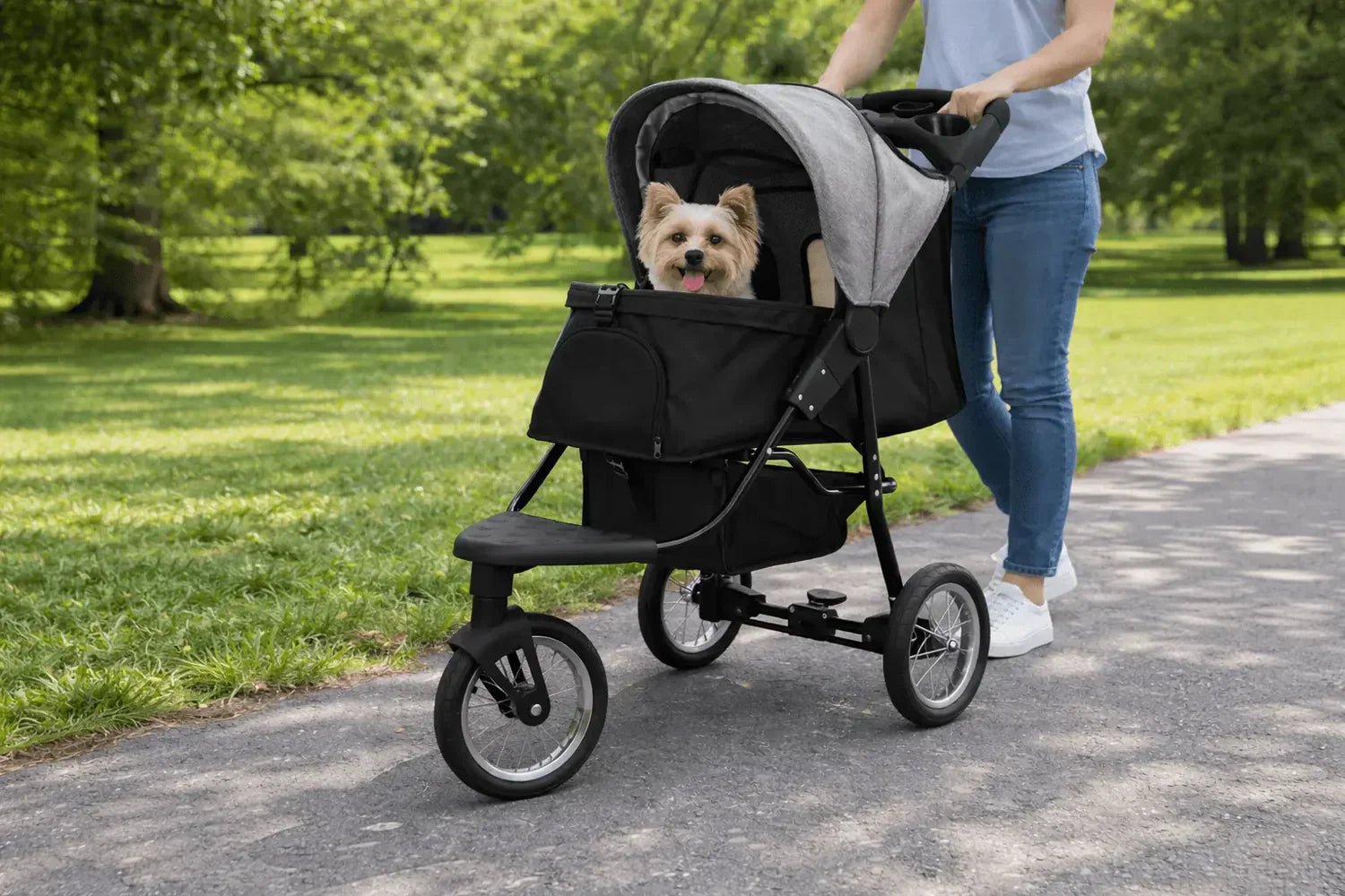 Een stijlvolle hondenbuggy met een grijze kap en zwarte basis, waarin een blije hond comfortabel zit, op een pad in het park