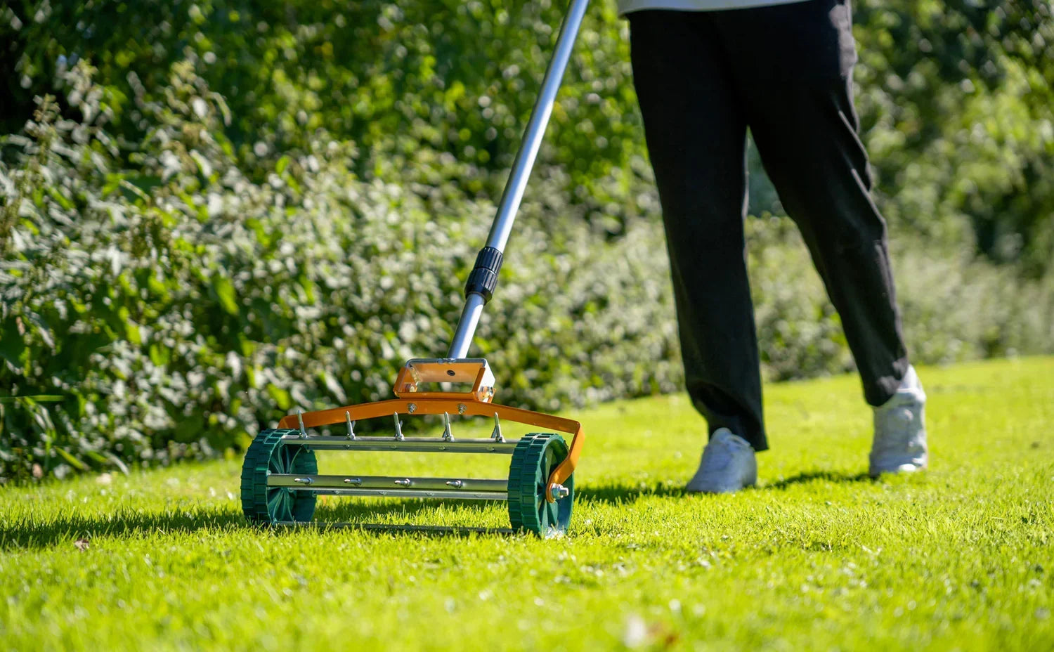 Een persoon met een grasmaaier met groene wielen en een oranje handvat, die een weelderig, groen gazon maait in de lente