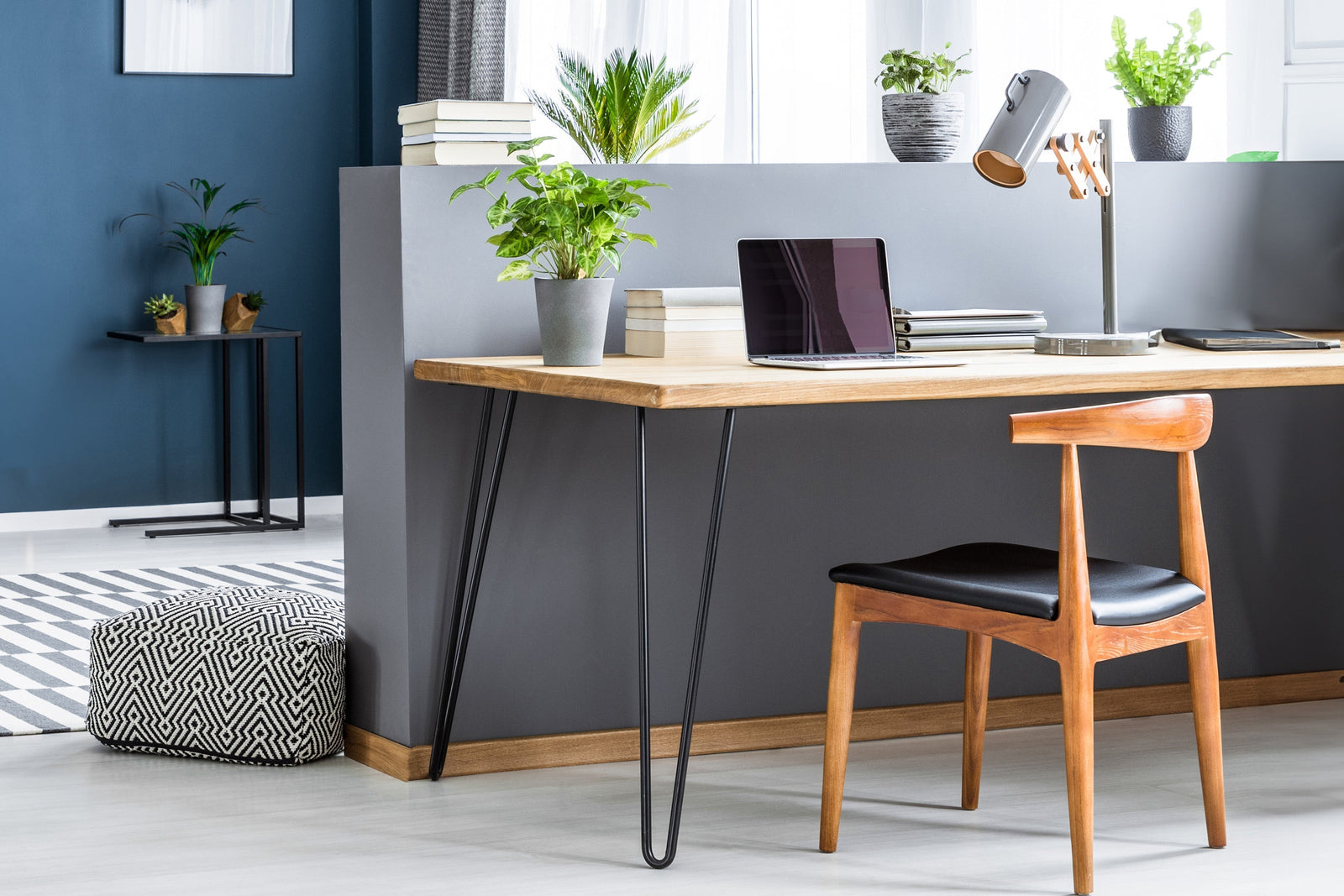 Een moderne houten tafel met hairpin poten, een zwarte stoel, planten in potten en een laptop op een stijlvolle werkplek
