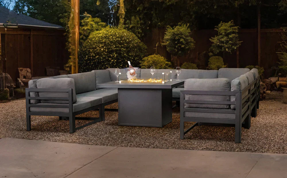 Moderne aluminium tuinset met grijze kussens, een vierkante tafel en sfeervolle verlichting in een groene tuinomgeving