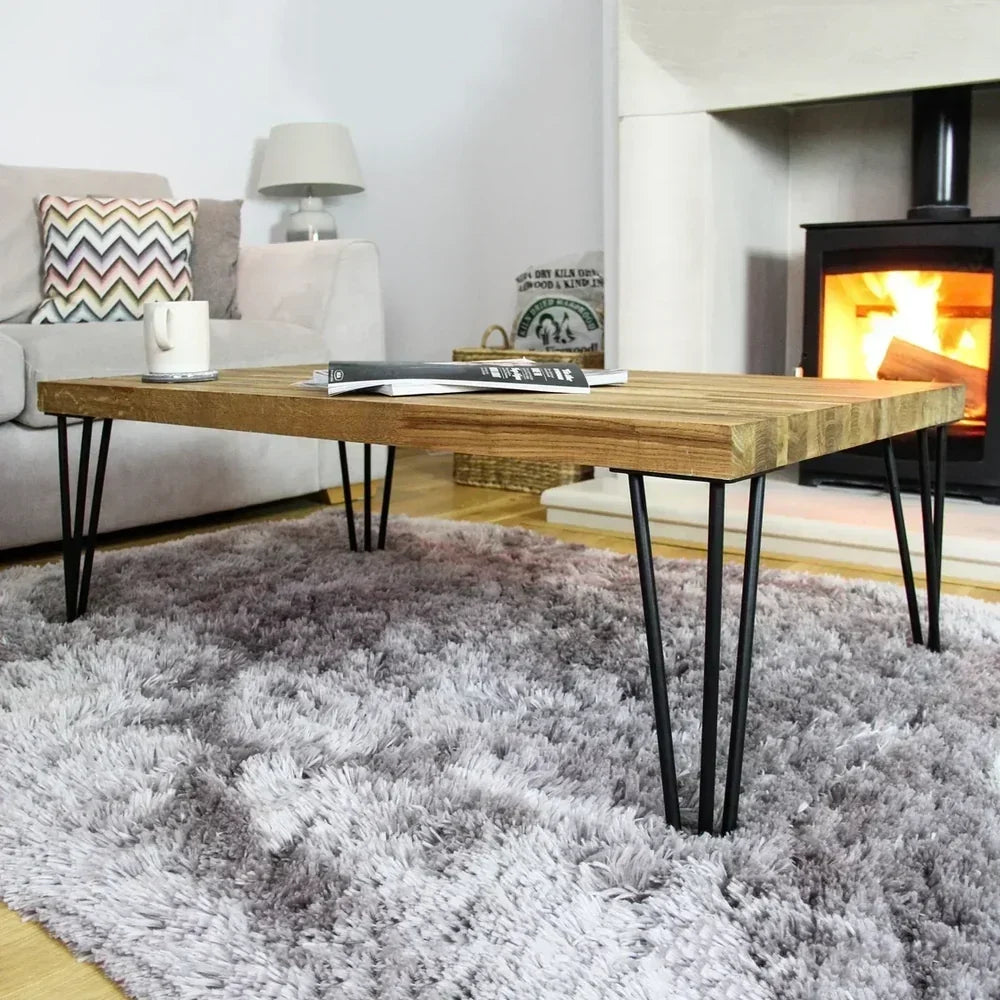 Een houten salontafel met haarspeldpoten, geplaatst op een zachte, grijze vloerkleed, met een gezellige open haard op de achtergrond