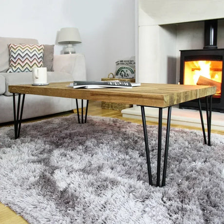 Een houten salontafel met haarspeldpoten, geplaatst op een zachte, grijze vloerkleed, met een gezellige open haard op de achtergrond