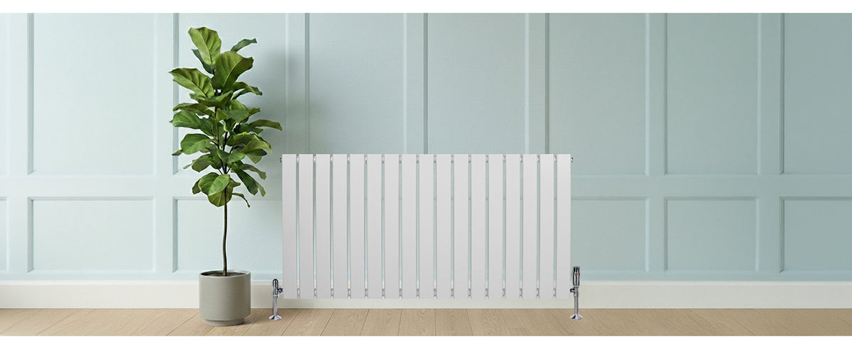 Witte verticale radiator met strakke lijnen, geplaatst tegen een lichtblauwe muur, naast een groene plant in een moderne pot