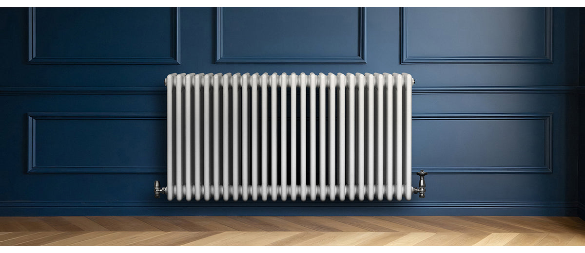 Witte radiator met een modern, gestreept ontwerp tegen een diepblauwe wand, geplaatst op een houten vloer met een warme tint