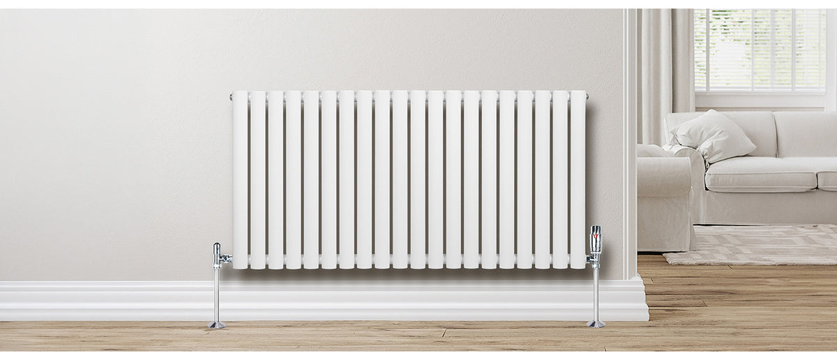Witte verticale radiator met rechte lijnen, geplaatst tegen een lichte muur, met een houten vloer en een comfortabele bank op de achtergrond