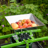 Draagbare fruitmolen met slinger, groene metalen structuur, roestvrijstalen kom vol met rode appels, ideaal voor fruitverwerking