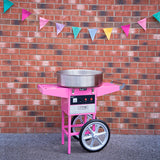 Roze suikerspinmachine met een glanzende metalen kom, geplaatst voor een bakstenen muur versierd met kleurrijke vlaggetjes