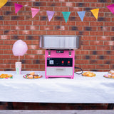 Roze suikerspinmachine op een tafel met een witte tafelkleed, versierd met kleurrijke vlaggetjes en lekkernijen zoals cupcakes en suikerspin