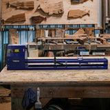 Houtdraaibank in diepblauwe kleur met accessoires, geplaatst op een houten werkbank omringd door diverse houtsoorten en gereedschap