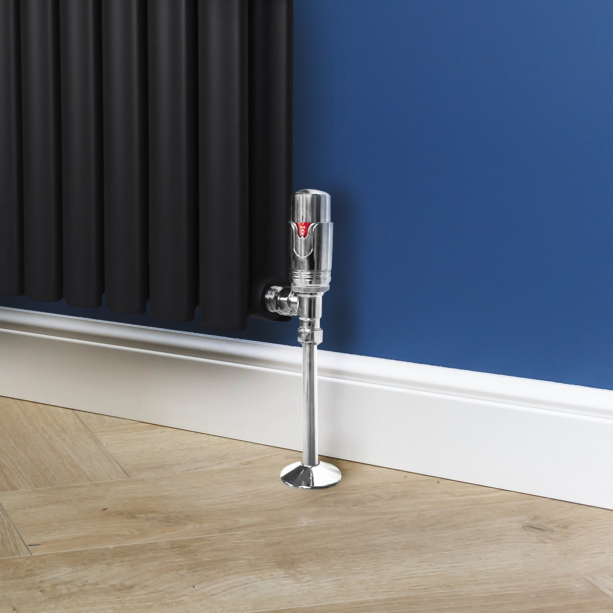 Chroom thermostatische radiatorkraan met glanzende afwerking, geplaatst naast een zwarte radiator op een houten vloer tegen een blauwe muur