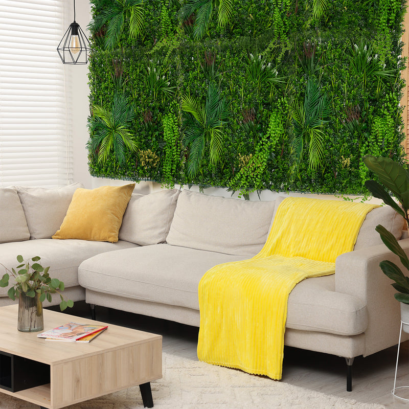 Een lichte, moderne woonkamer met een beige bank, een felgele plaid, een houten salontafel en een groene plantenwand als achtergrond