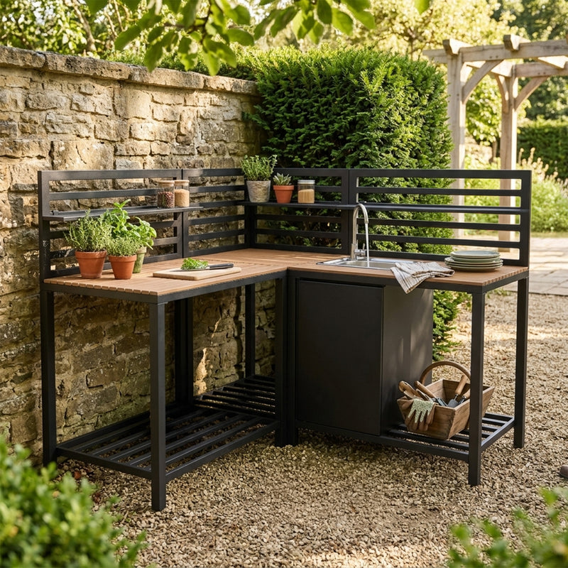 Moderne buitenkeuken met zwart metalen frame, houten werkblad, plantenpotten en een spoelbak, geplaatst op een grindvloer in een groene tuin