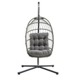 Grijze rotan hangstoel met een comfortabele, zachte kussen en een stevige metalen standaard, perfect voor binnen en buiten