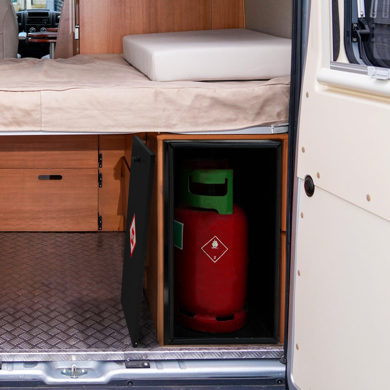 Een gasfles in een zwarte kast onder een bed in een camper, met een houten interieur en een metalen vloerbedekking
