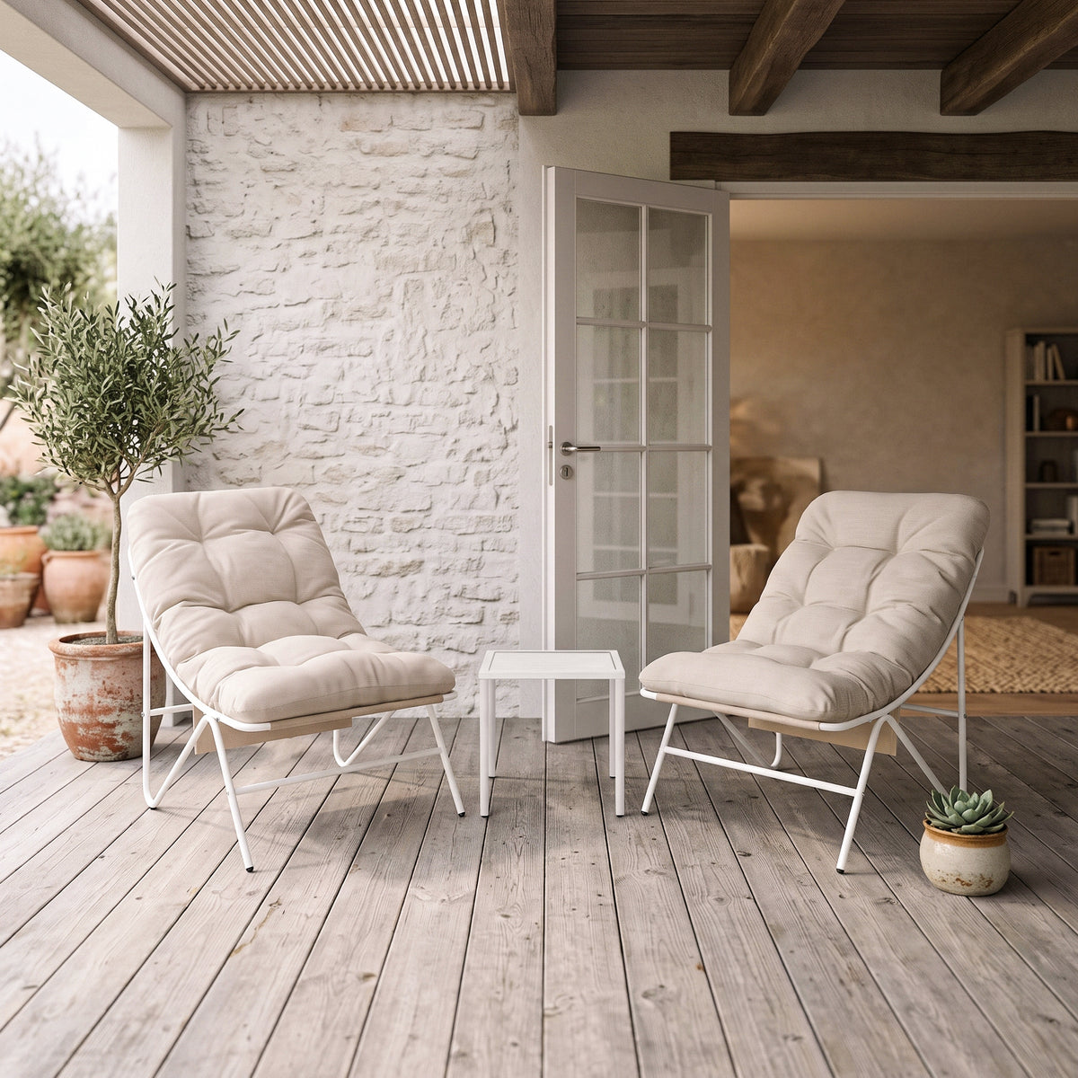 Twee lichte, comfortabele stoelen met kussens op een houten terras, omringd door planten en een kleine tafel in een sfeervolle setting