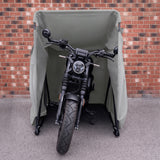 Zwart motorfiets met een moderne uitstraling, beschermd door een groene hoes, geplaatst tegen een bakstenen muur
