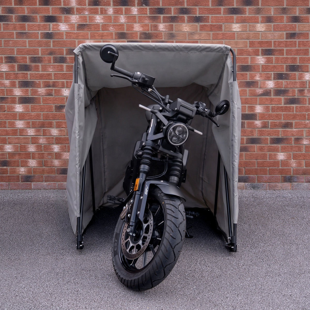 Zwarte motorfiets met een robuuste uitstraling, geparkeerd onder een grijze beschermhoes tegen een bakstenen muur