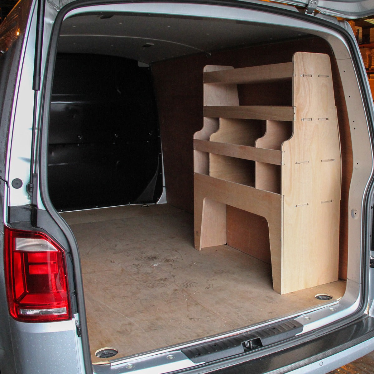 Zwarte bestelwagenbekleding en houten rek in een VW Transporter, met een strakke, moderne afwerking en een ruime indeling