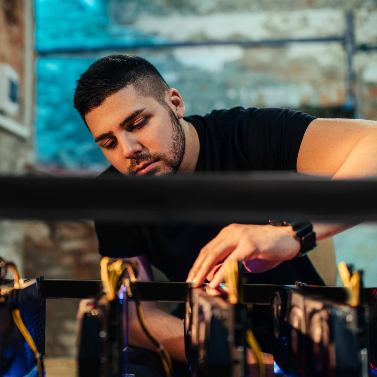 Een man in zwart T-shirt werkt zorgvuldig aan een 6-8 GPU mining rig frame, met zichtbare grafische kaarten en kabels in een industriële omgeving