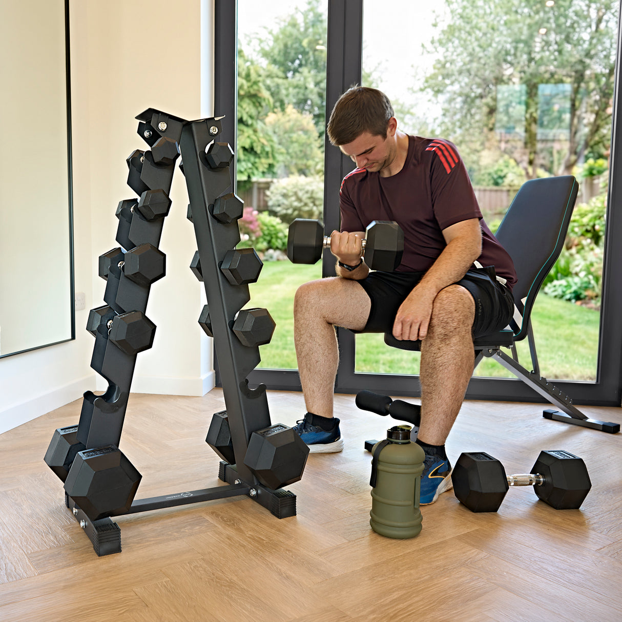 Zwart 6-laags dumbbellrek met hexagonale gewichten, een man in sportkleding traint in een lichte, moderne ruimte met grote ramen