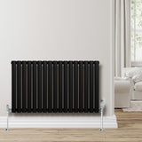 Ovale zwarte design radiator met één kolom, 600 mm x 1020 mm, met haakse thermostaatkraan, geplaatst tegen een lichte muur