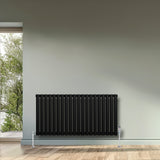 Zwarte ovale design radiator met één kolom, 600 mm x 1200 mm, inclusief haakse thermostaatkraan, geplaatst tegen een lichte muur