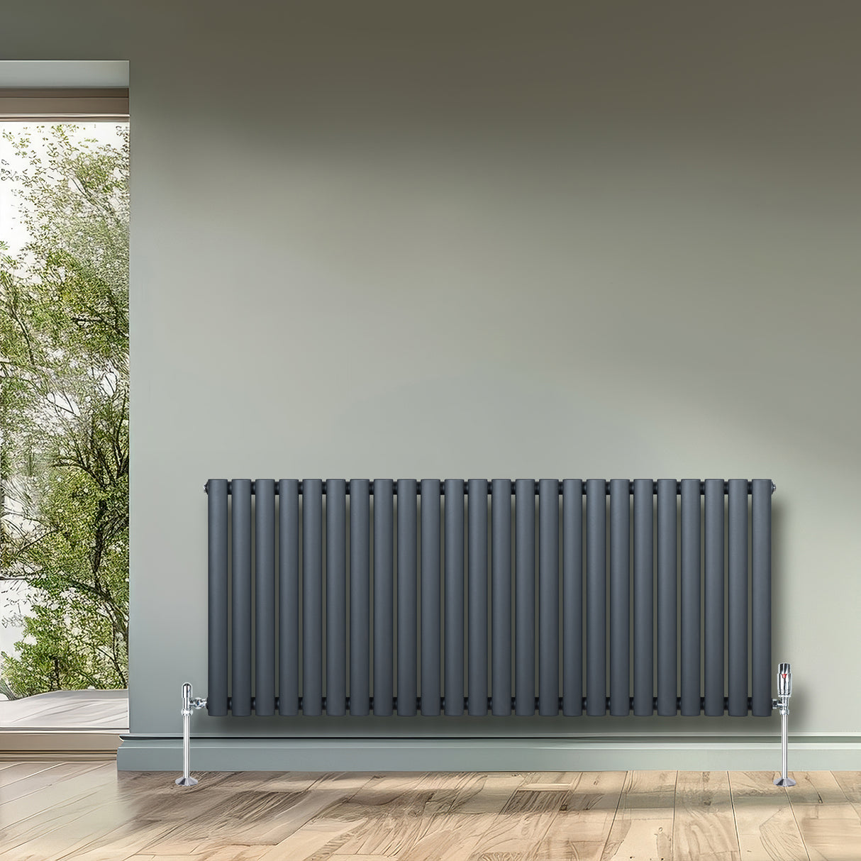 Ovale design radiator in antraciet grijs, 600 mm x 1440 mm, met een haakse thermostaatkraan en verticale kolommen, geplaatst tegen een muur