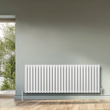 Ovale witte designradiator met één kolom, 600 mm x 1620 mm, geplaatst tegen een groene muur, inclusief haakse thermostaatkraan
